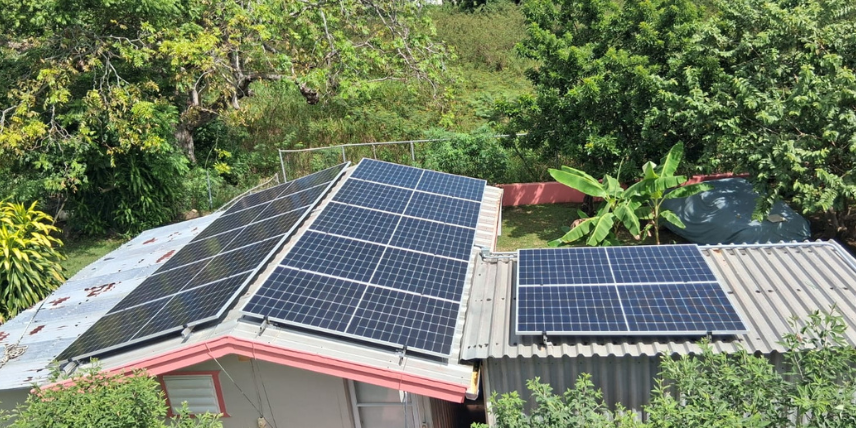 Paneles solares instalados sobre techo de zinc en casa residencial en Puerto Rico, rodeada de vegetación tropical, mostrando solución de energía solar adaptada a la isla
